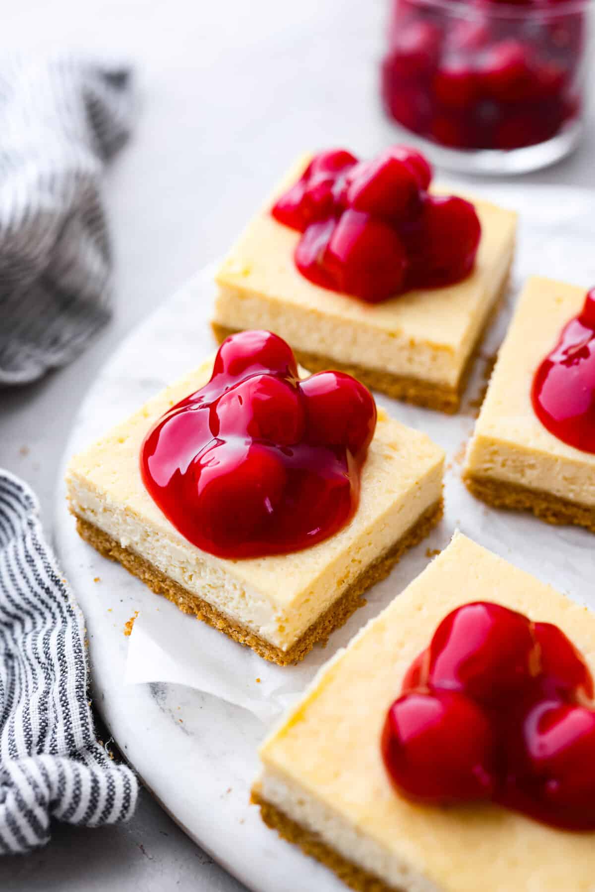 Sliced cheesecake bars topped with cherry pie filling on a white serving platter.