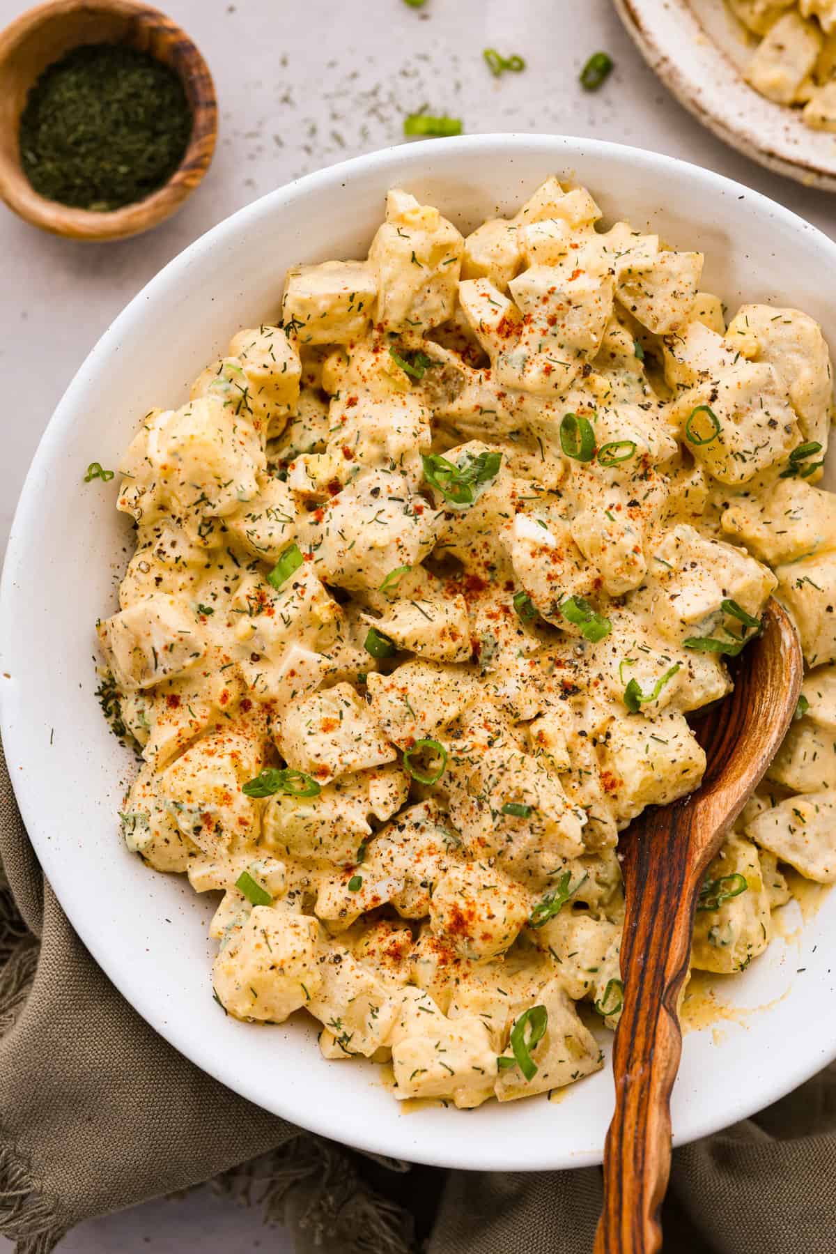 Potato salad served in a white bowl and garnished with green onions, paprika, and herbs.