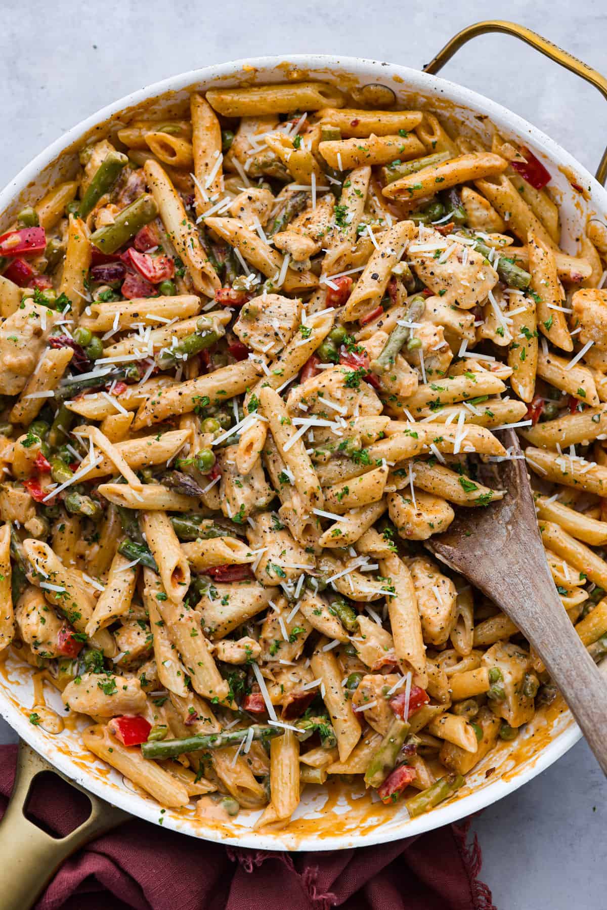 Top-down view of chipotle pasta in a white skillet with a gold handle. It is being stirred with a wooden spoon.