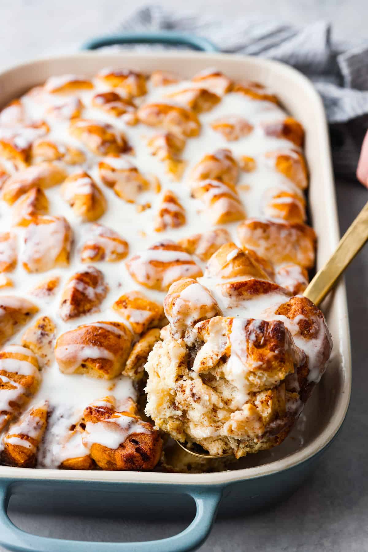 A casserole dish with cinnamon roll casserole baked and ready to eat. One slice being dished out with a gold spoon.