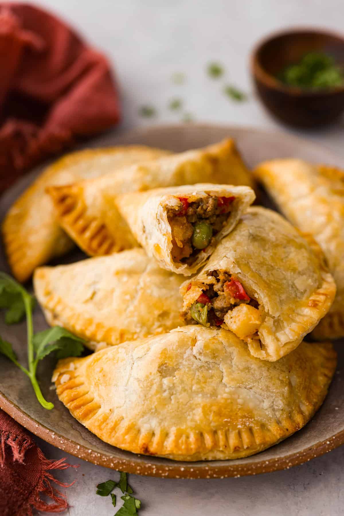 Air fryer empanadas on a serving dish. One is broken in half so you can see the filling.