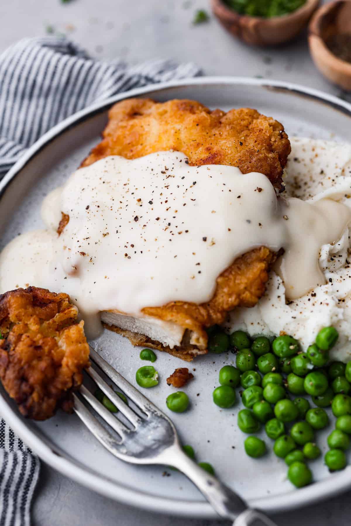 Closeup of country fried chicken covered with gravy and served with peas.