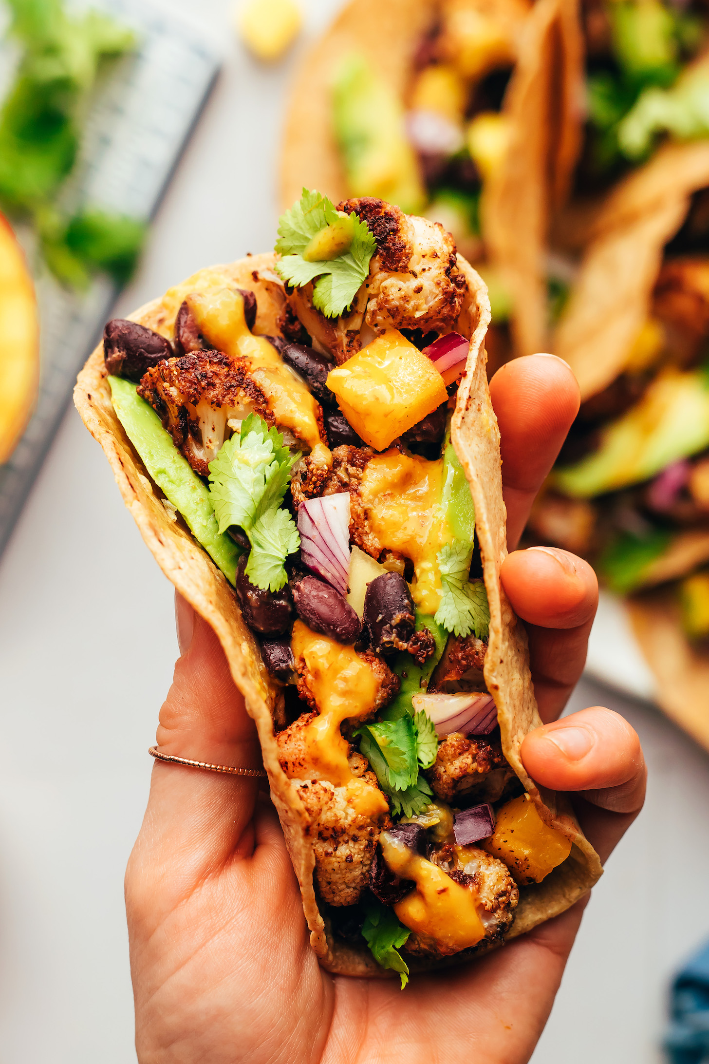 Holding a jerk cauliflower taco stuffed with mango, red onion, avocado, and cilantro