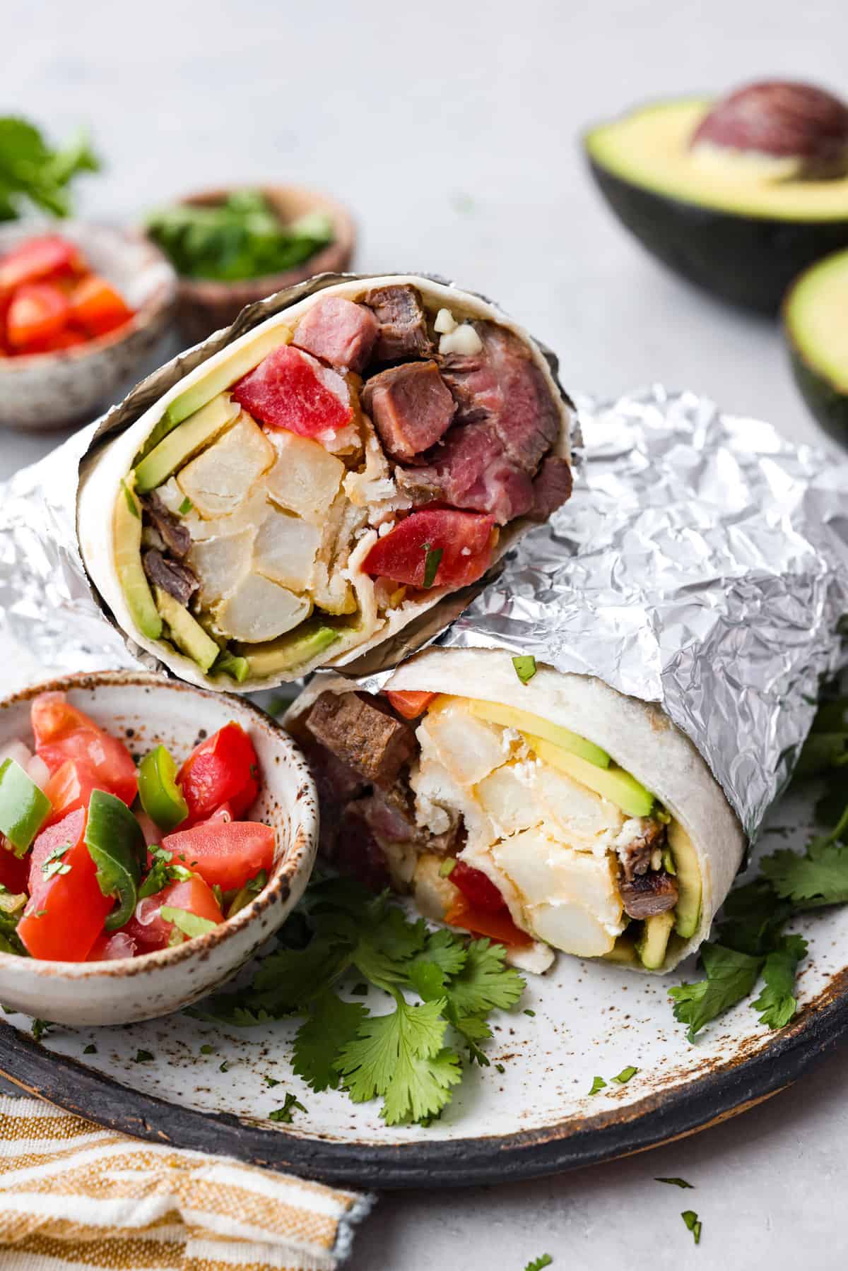 A california burrito wrapped in tinfoil and sliced in half.