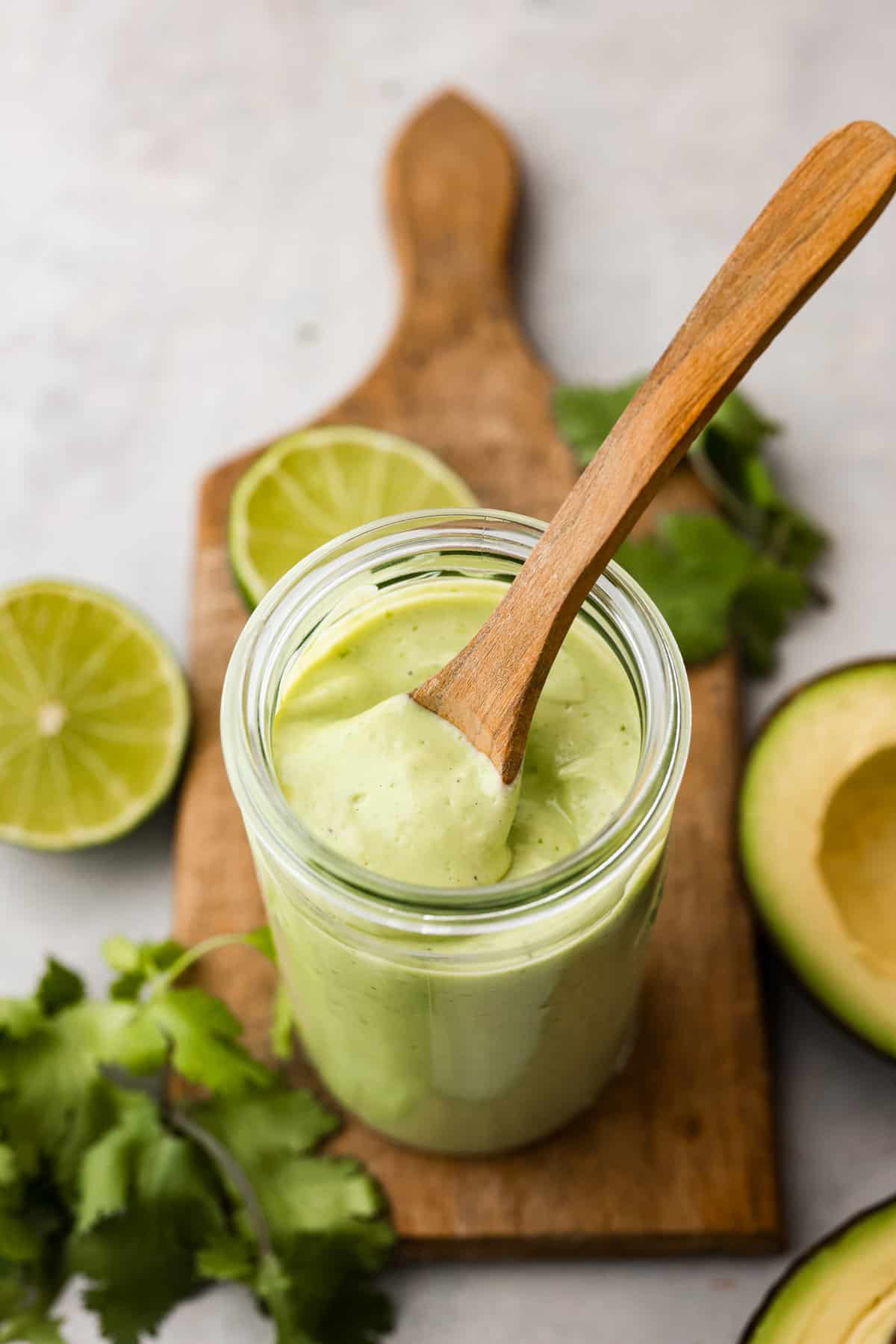 Overhead view of avocado dressing in glass jar with wood spoon sticking out.